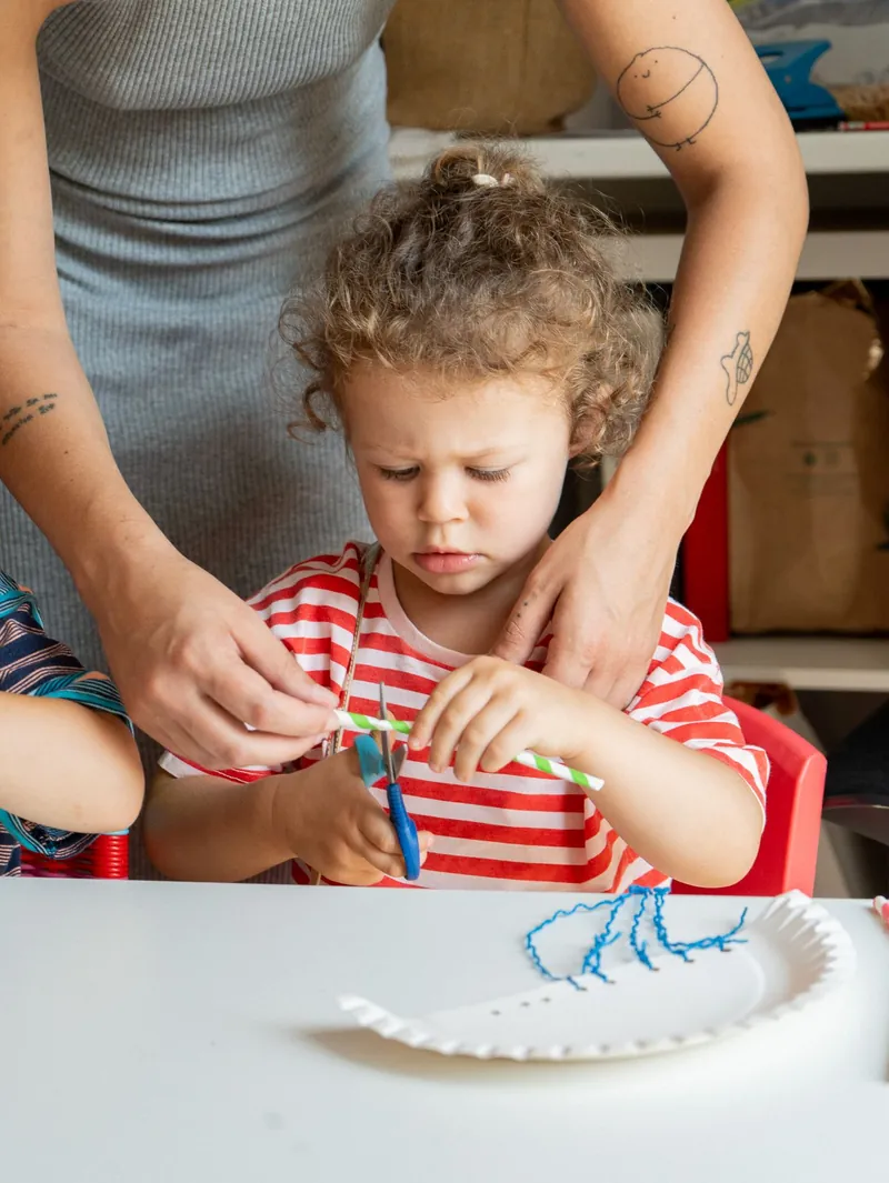 A Handprints teacher guiding a child's hands through a craft