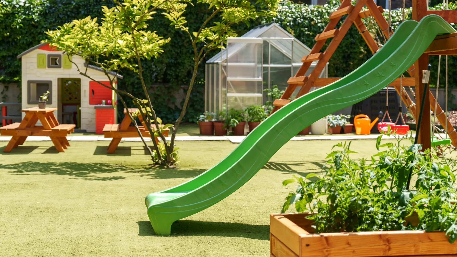 The school garden in summer, with the slide, greenhouse, and planting beds