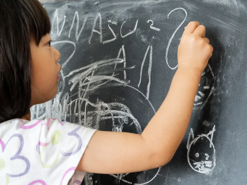 A Preschool child writing her first letters on the classroom chalkboard