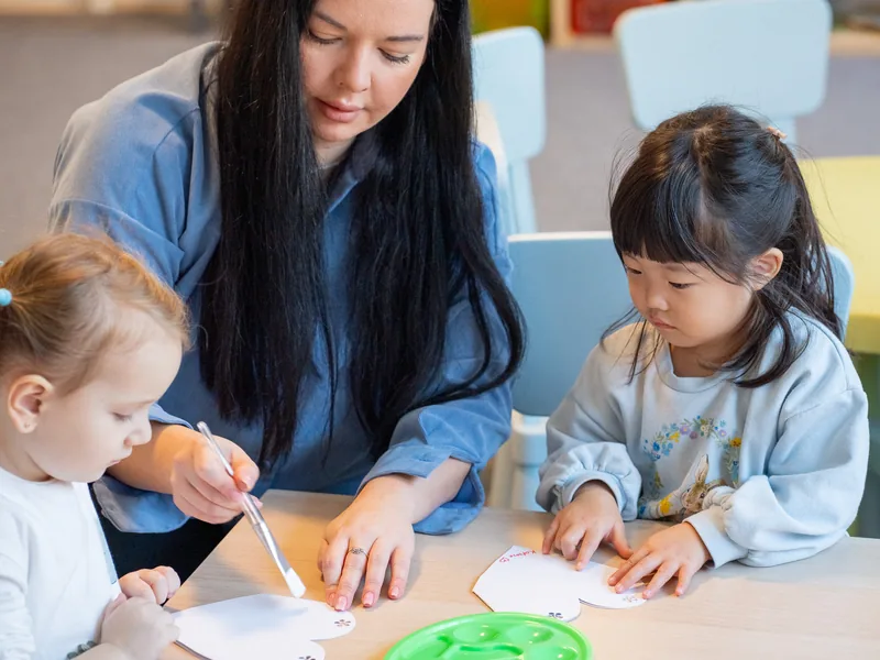 A teacher working with two children at the classroom table